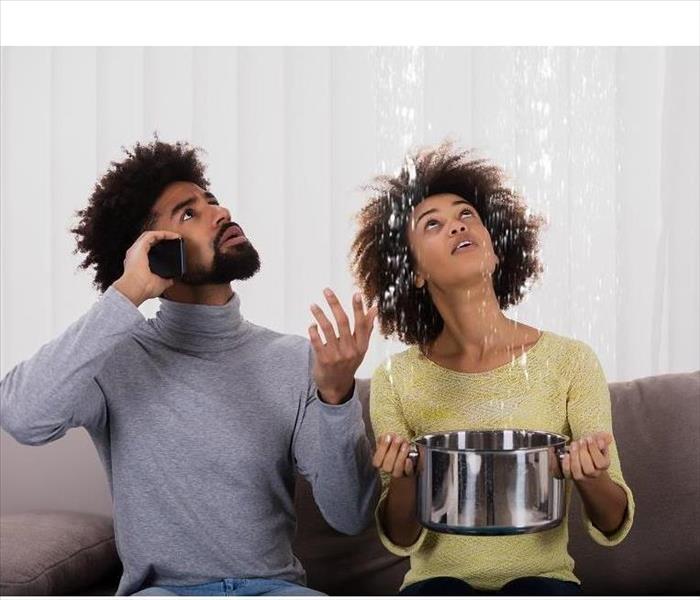 Image of 2 persons staring at a leak coming from the ceiling. 